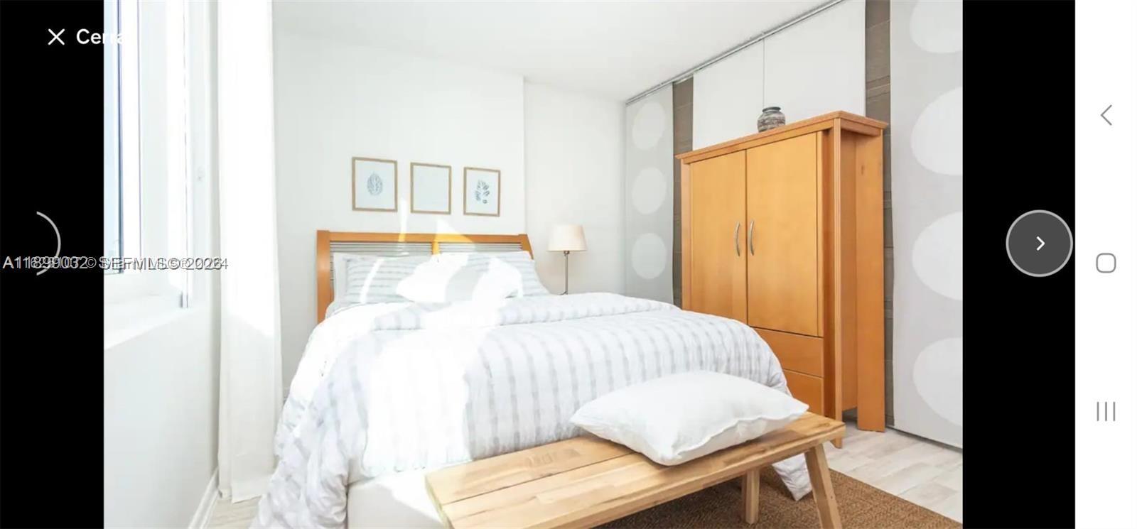 A bedroom features a bed with a striped comforter, a wooden wardrobe, and a bench — 2301 Collins Ave # 736, Miami Beach FL 33139, MIAMI BEACH, FL
