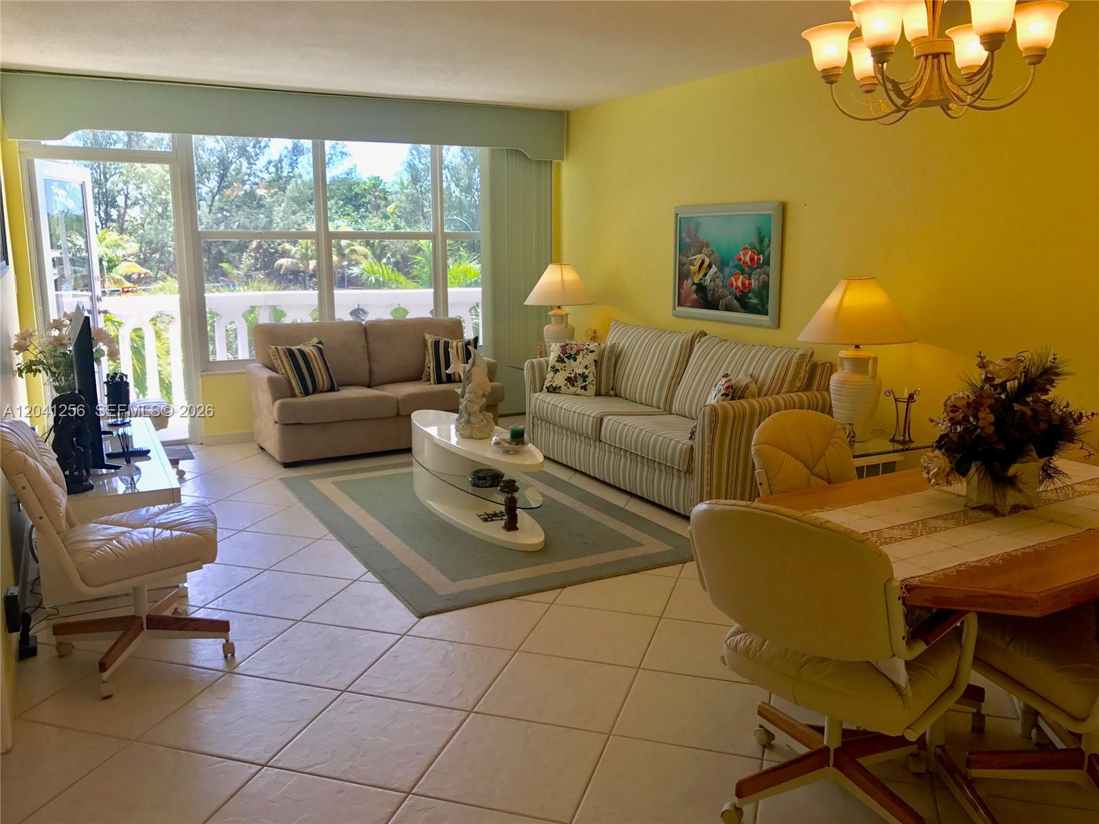 A living and dining area features yellow walls, tile flooring, and a balcony view — 3199 S Ocean Dr # 402, Hallandale Beach FL 33009, HALLANDALE BEACH, FL