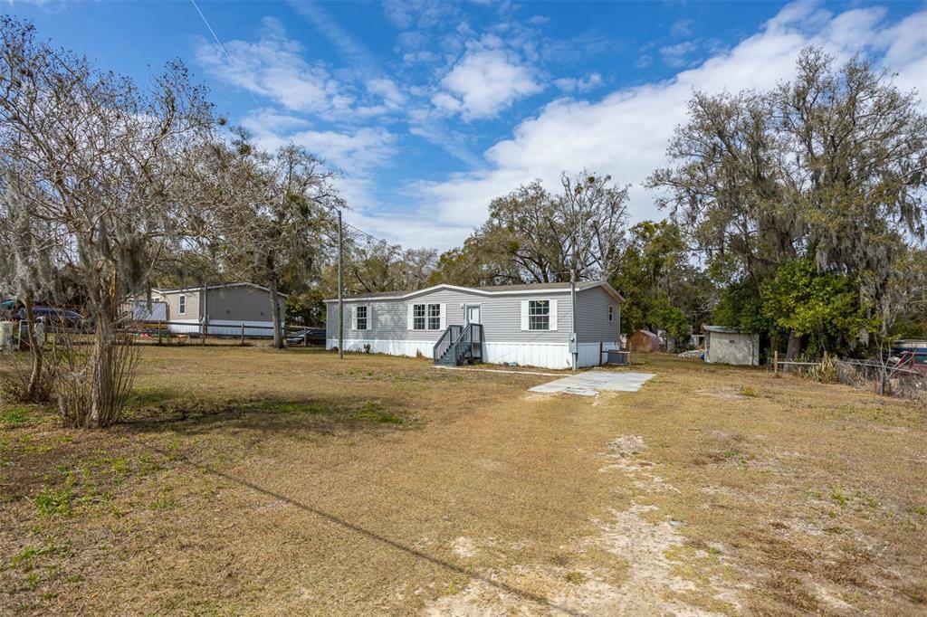 A single-story manufactured home sits on a large, grassy lot with mature trees — 40545 STEWART ROAD, ZEPHYRHILLS, FL