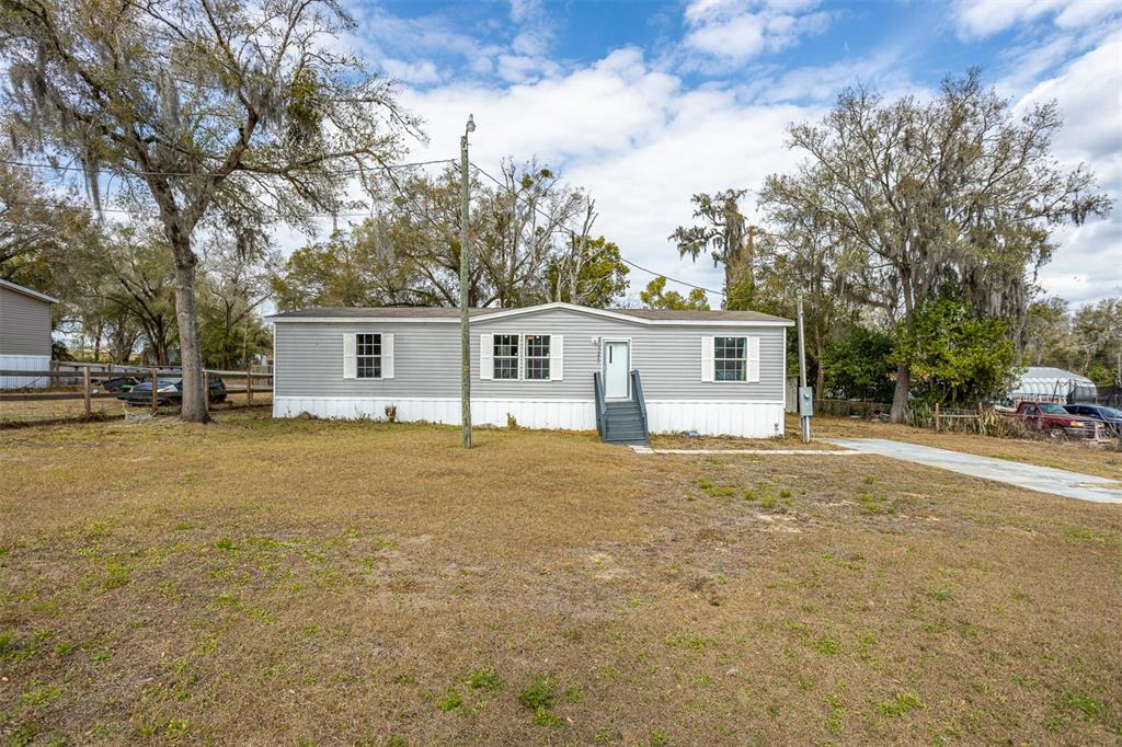 A gray single-wide mobile home sits on a grassy lot with mature trees — 40545 STEWART ROAD, ZEPHYRHILLS, FL