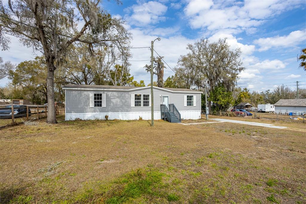 A single-story manufactured home with gray siding sits on a large, grassy lot — 40545 STEWART ROAD, ZEPHYRHILLS, FL