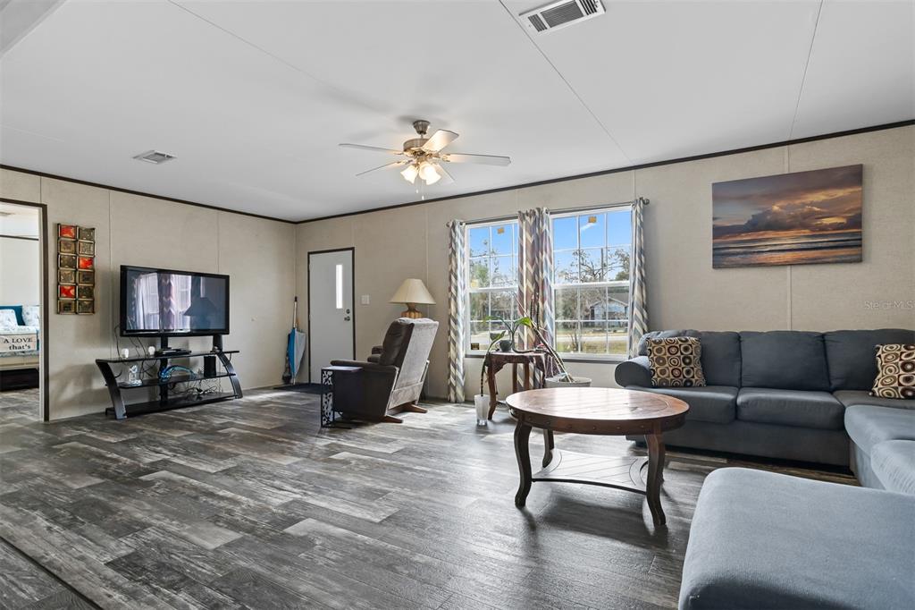 A living room features wood-look flooring, a ceiling fan, a sofa, and a television stand — 40545 STEWART ROAD, ZEPHYRHILLS, FL