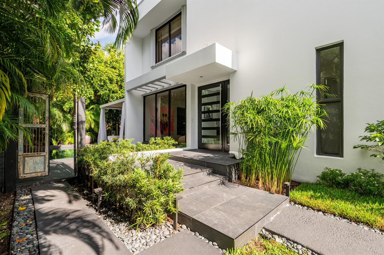 A modern white house exterior features a dark tiled entryway, glass door, and lush landscaping — 423 Chilean Avenue, Palm Beach FL 33480, PALM BEACH, FL