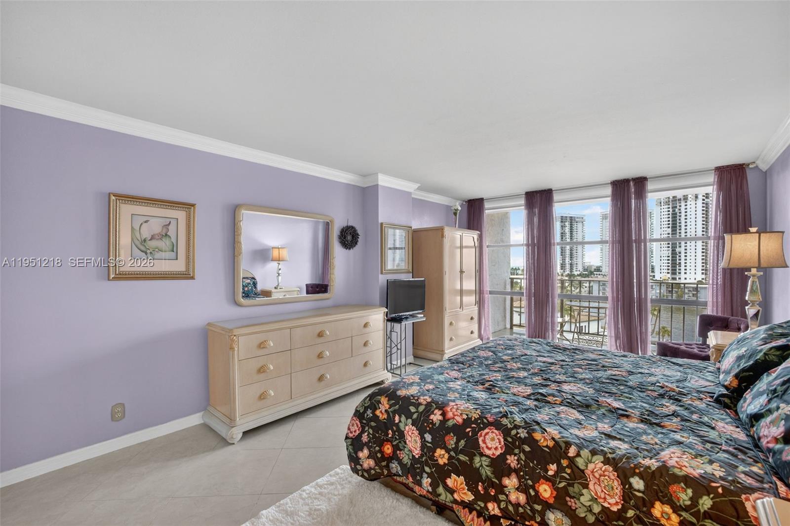 A bedroom with lavender walls, a floral bedspread, a dresser, and a balcony with city views — 1000 Parkview Dr # 806, Hallandale Beach FL 33009, HALLANDALE BEACH, FL