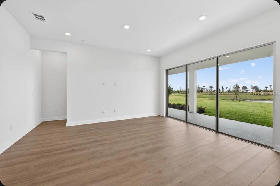 An empty room with wood-look flooring, recessed lighting, and large sliding glass doors overlooking grass — 853 TASSLEFLOWER TRAIL, ST CLOUD, FL
