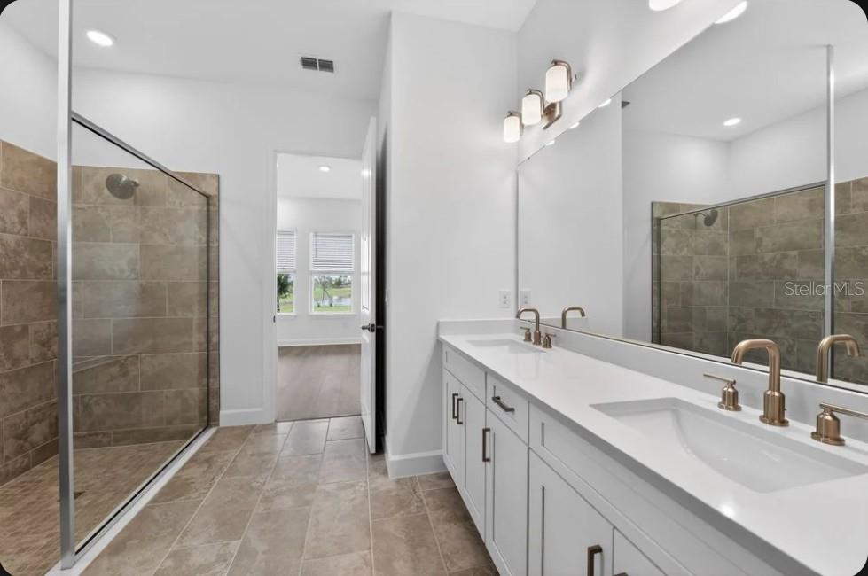 A bathroom with a glass-enclosed shower, double vanity with white cabinets, and large wall mirror — 853 TASSLEFLOWER TRAIL, ST CLOUD, FL