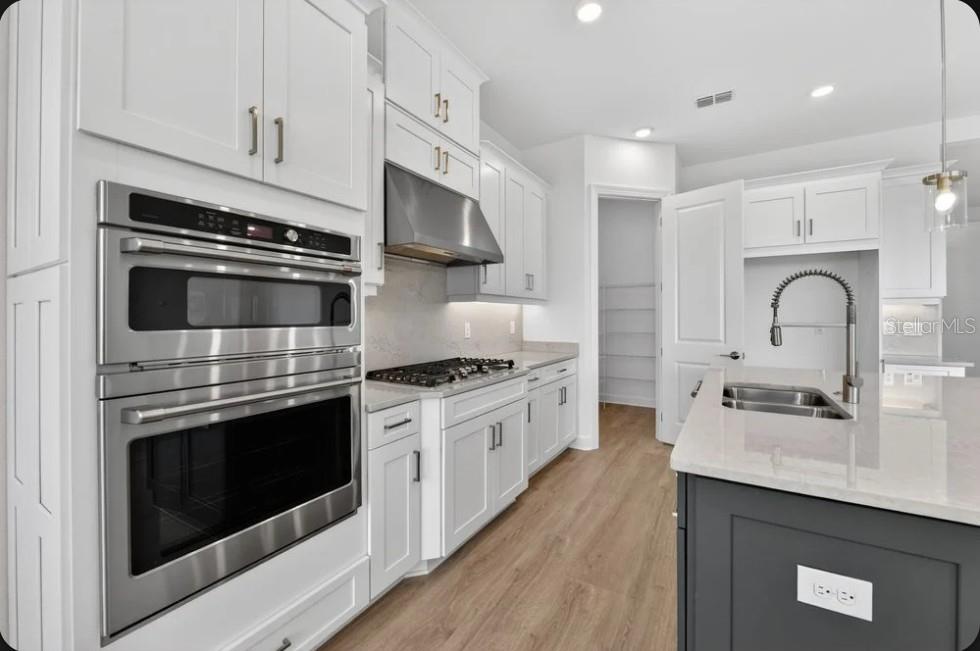 A modern kitchen features white cabinetry, stainless steel appliances, a gas cooktop, and a dark island — 853 TASSLEFLOWER TRAIL, ST CLOUD, FL