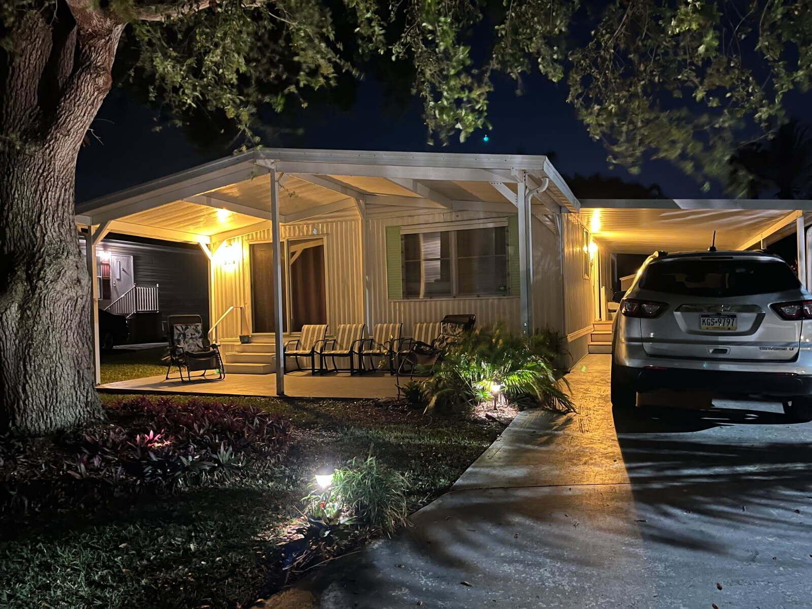 A mobile home exterior at night featuring a covered patio, carport, and a parked SUV — 304 Mockingbird Avenue, Fort Pierce FL 34982, FORT PIERCE, FL
