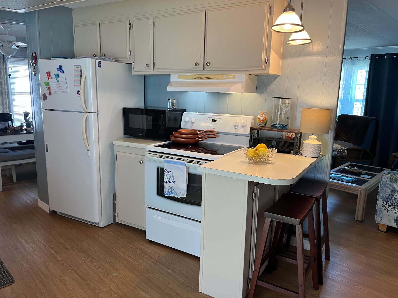 A kitchen features white appliances, light-colored cabinets, a small breakfast bar, and wood-look flooring — 304 Mockingbird Avenue, Fort Pierce FL 34982, FORT PIERCE, FL