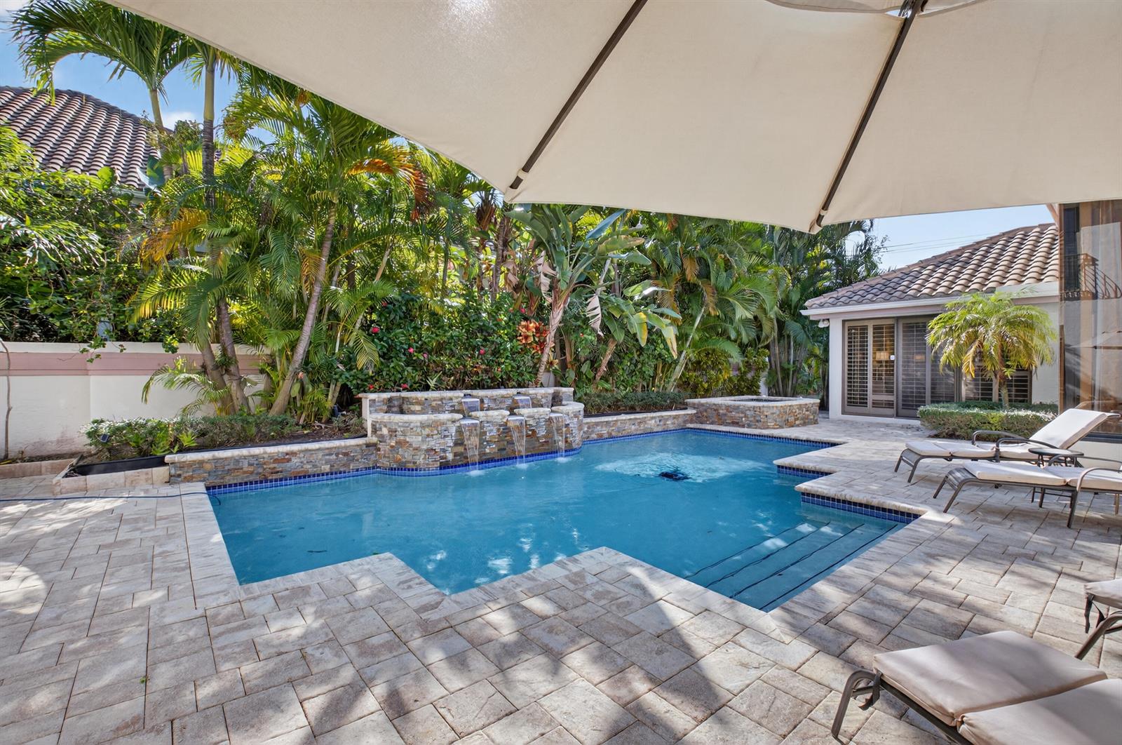 A swimming pool with a stone waterfall feature sits on a paved patio with lounge chairs — 2629 NW 64th Place, Boca Raton FL 33496, BOCA RATON, FL