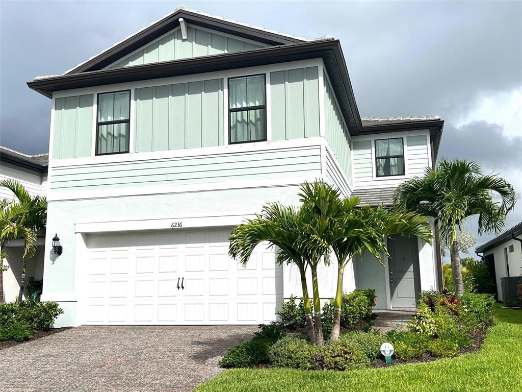A two-story house features a white garage, light green siding, and palm trees in front — 6236 BAYWOOD COURT, LAKEWOOD RANCH, FL