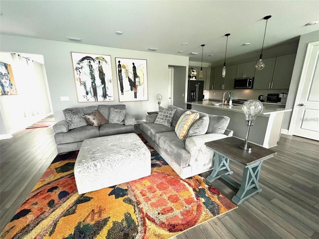 A living room with gray sofas, a patterned rug, and an open kitchen with island seating — 6236 BAYWOOD COURT, LAKEWOOD RANCH, FL