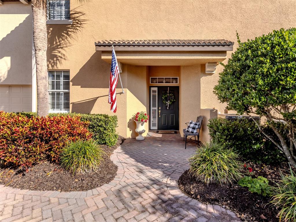 A paved walkway leads to the front entrance of a tan house with a flag — 114 BELLA VISTA TERRACE UNIT 6B, NORTH VENICE, FL