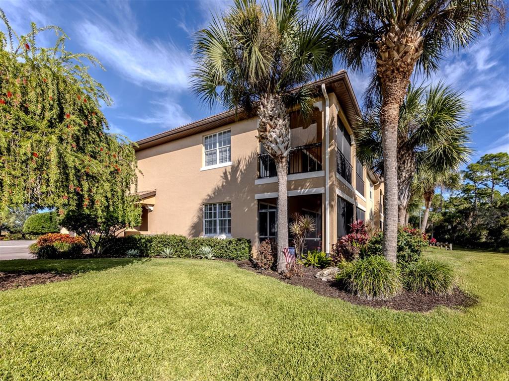 A two-story tan stucco building features screened balconies, palm trees, and a landscaped lawn — 114 BELLA VISTA TERRACE UNIT 6B, NORTH VENICE, FL