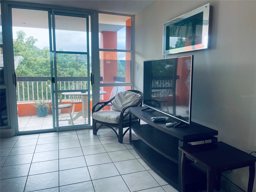 A living room with tiled floors, a television on a stand, and a balcony view — Cond.180 Carretera 194 PR 180- CARR. ESTATAL NO. 194 ESTATES UNIT Q-206, FAJARDO, PR