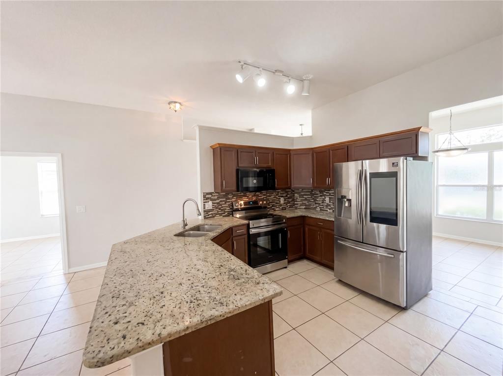 A kitchen features dark wood cabinets, granite countertops, stainless steel appliances, and tile flooring — 62 CORDONA DRIVE, KISSIMMEE, FL