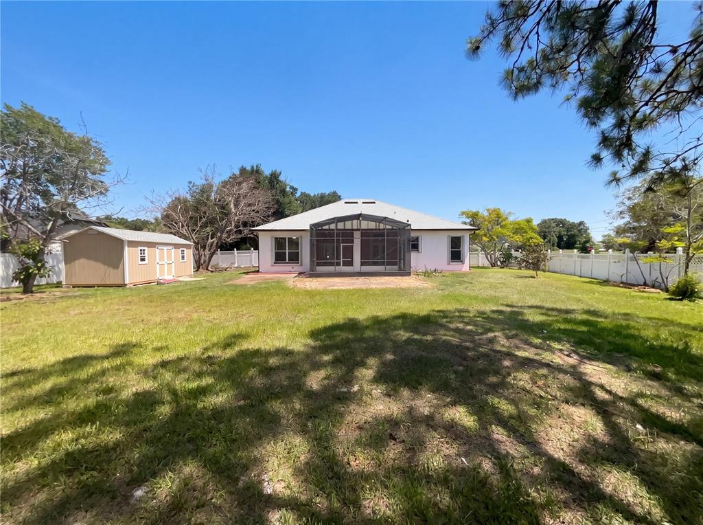 A backyard view of a single-story house with a screened-in porch and a storage shed — 62 CORDONA DRIVE, KISSIMMEE, FL