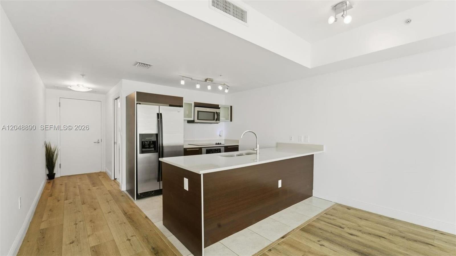 A modern kitchen features a white island, stainless steel appliances, and wood-look flooring — MIAMI, FL