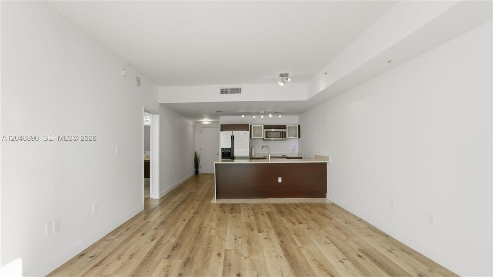 An open-concept living area features light wood-look flooring and a kitchen with dark cabinetry — MIAMI, FL