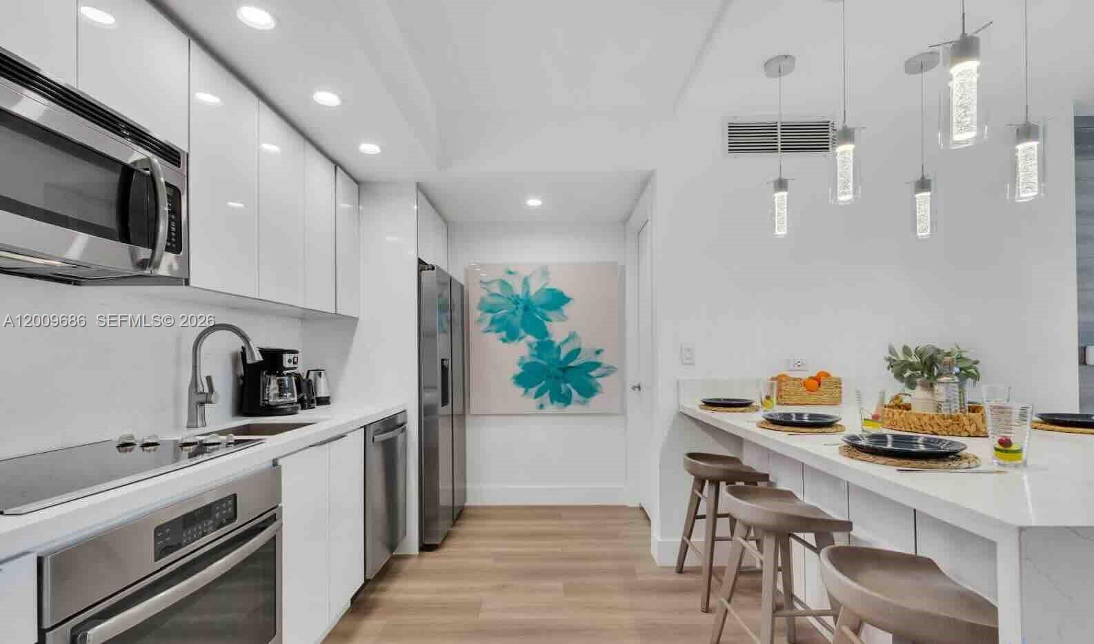 A modern kitchen features white cabinetry, stainless steel appliances, and a breakfast bar with stools — 2602 E Hallandale Beach Blvd # R506, Hallandale Beach FL 33009, HALLANDALE BEACH, FL