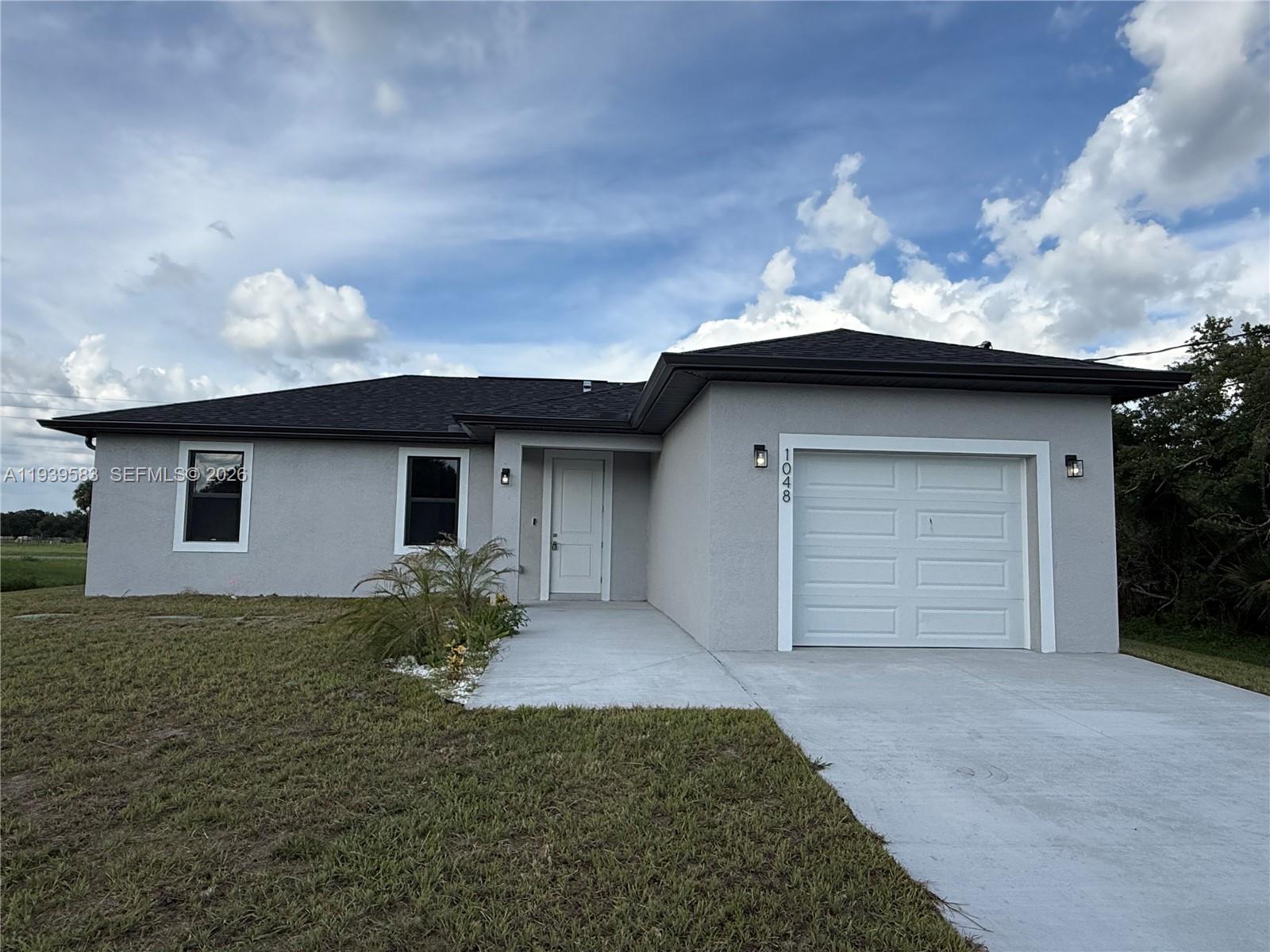 A single-story gray house features a white garage door, a front entrance, and a lawn — 1048 Jay Ct, La Belle FL 33935, LA BELLE, FL