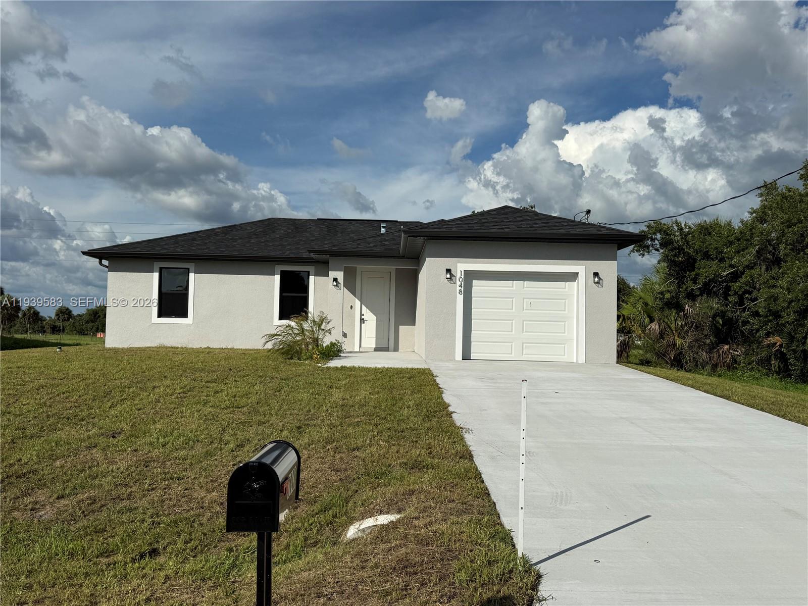 A single-story house with a gray stucco exterior, a dark roof, and a concrete driveway — 1048 Jay Ct, La Belle FL 33935, LA BELLE, FL