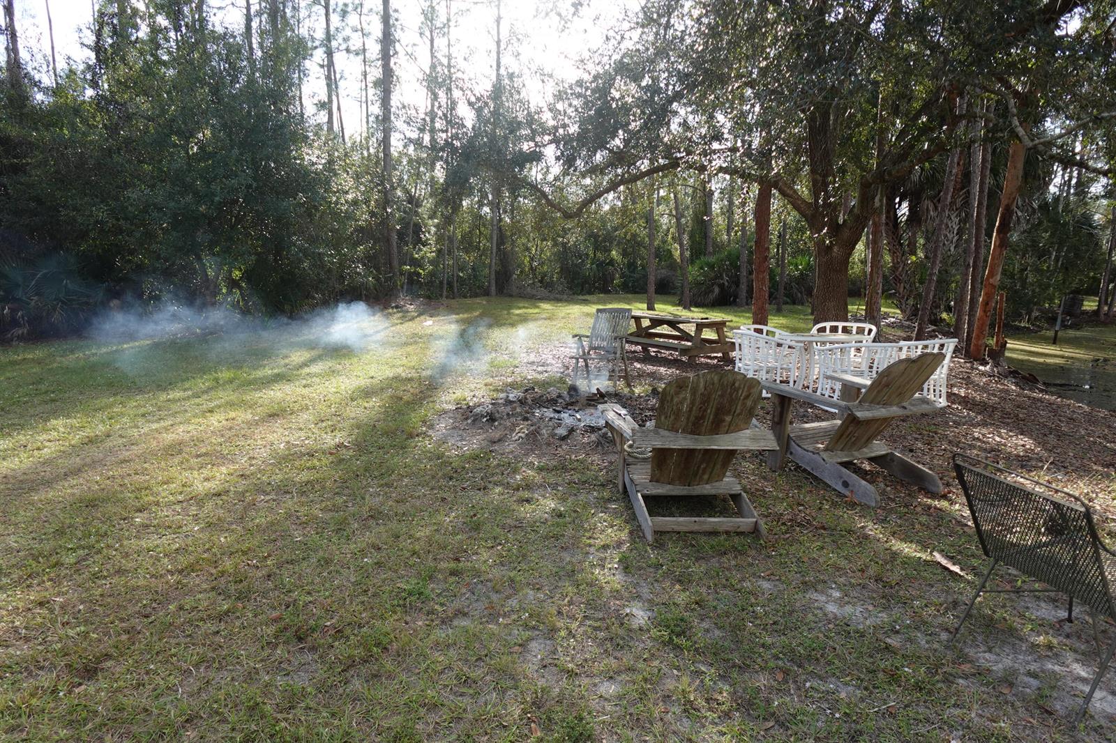 A backyard fire pit area features wooden Adirondack chairs and a picnic table near woods — 32801 N Us-441 Lot 187, Okeechobee FL 34972, OKEECHOBEE, FL