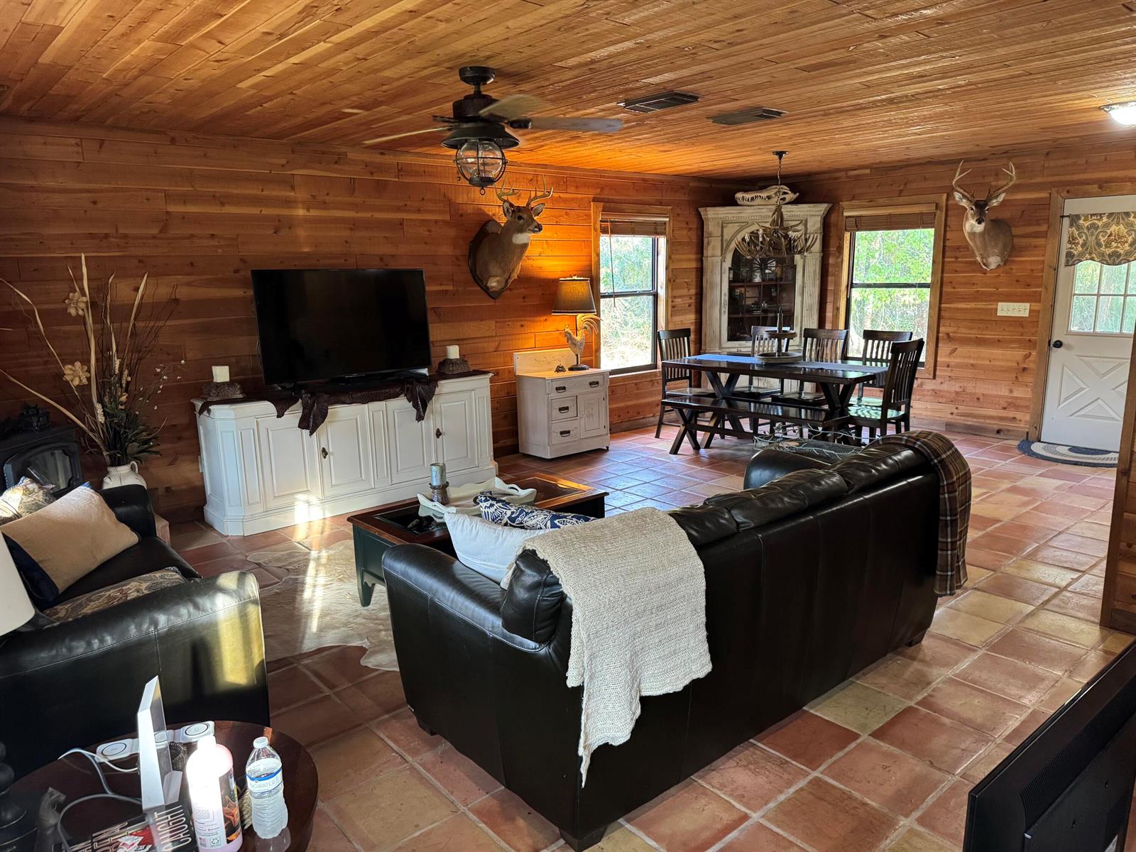 A rustic living and dining area features wood-paneled walls, tile flooring, and two deer mounts — 32801 N Us-441 Lot 187, Okeechobee FL 34972, OKEECHOBEE, FL