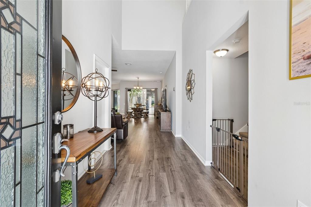 A view from an entryway looking down a hallway with wood-look flooring toward a dining area — 5401 LOOKOUT PASS, WESLEY CHAPEL, FL