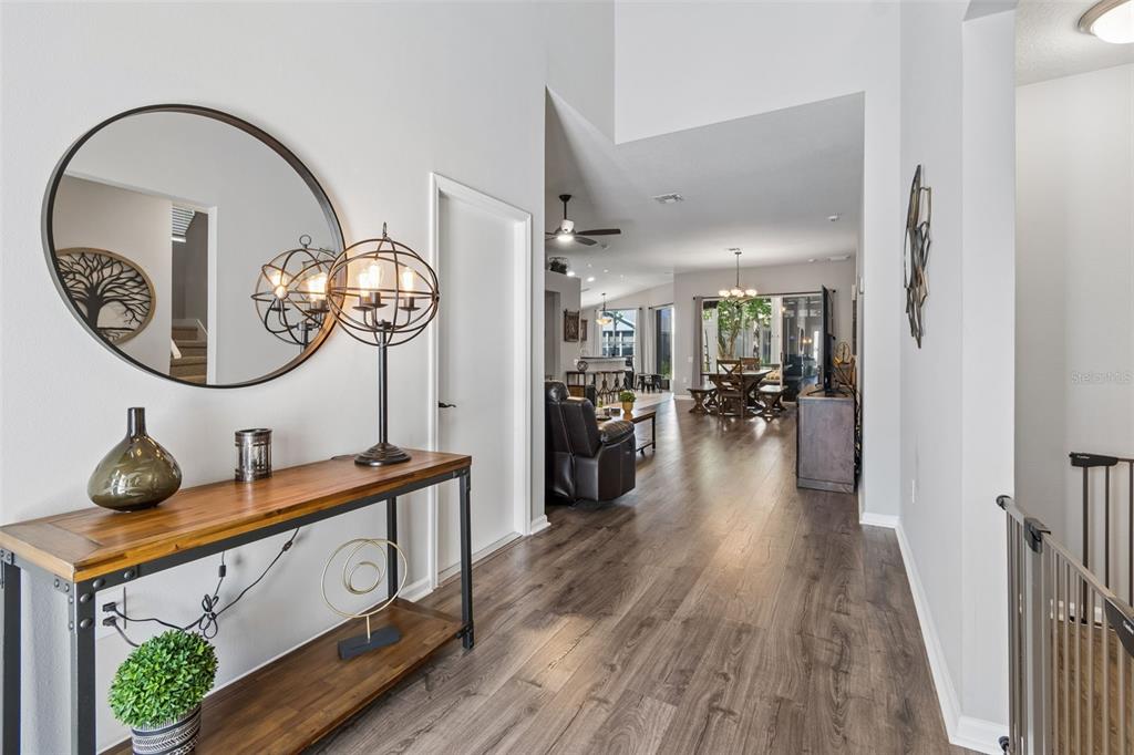 A foyer with a wood console table and round mirror leads into an open-concept living area — 5401 LOOKOUT PASS, WESLEY CHAPEL, FL