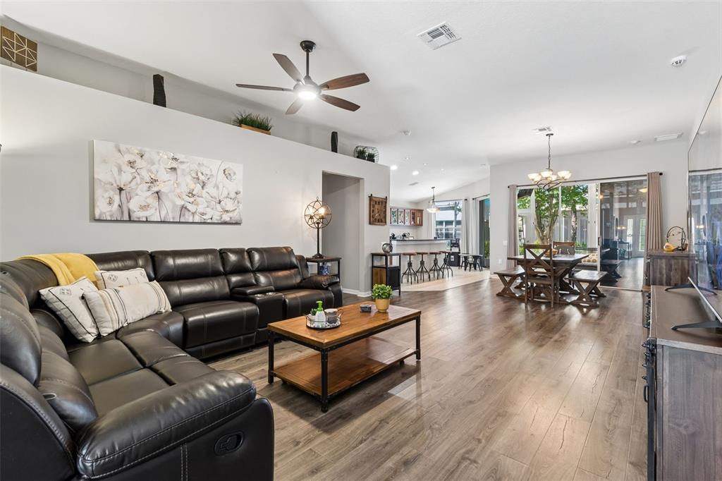 A living room with a dark leather sectional, wood coffee table, and open dining area — 5401 LOOKOUT PASS, WESLEY CHAPEL, FL
