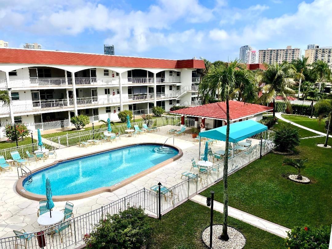 An outdoor swimming pool area with a covered patio and a multi-story apartment building — 580 Egret Dr # 308, Hallandale Beach FL 33009, HALLANDALE BEACH, FL