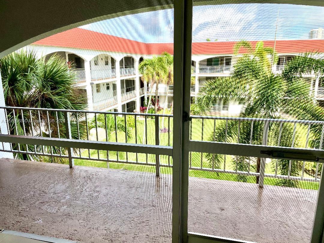 A view from a screened balcony overlooking a courtyard with palm trees and apartment buildings — 580 Egret Dr # 308, Hallandale Beach FL 33009, HALLANDALE BEACH, FL