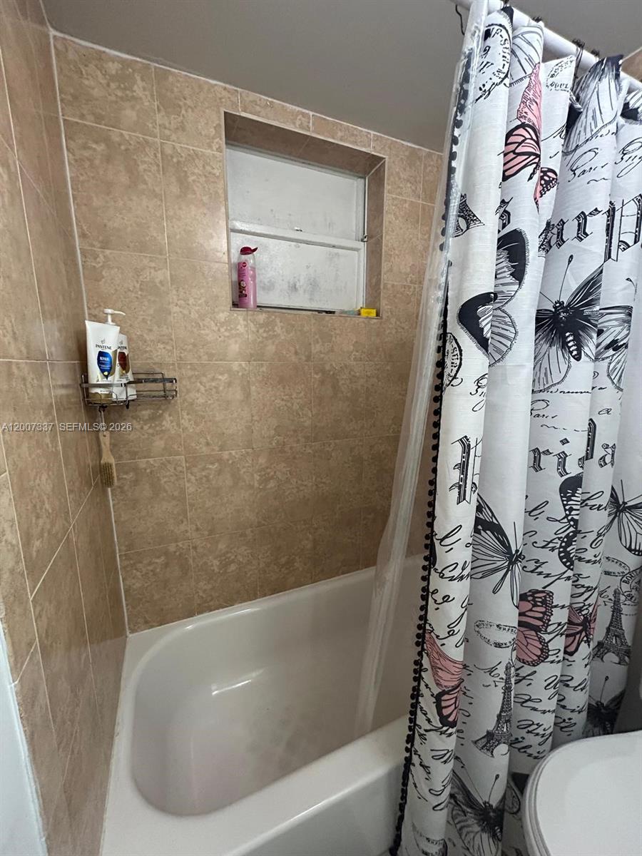 A bathroom features a white bathtub, tan tiled walls, and a butterfly-patterned shower curtain — 1100 NE 1st Ct # 104, Hallandale Beach FL 33009, HALLANDALE BEACH, FL