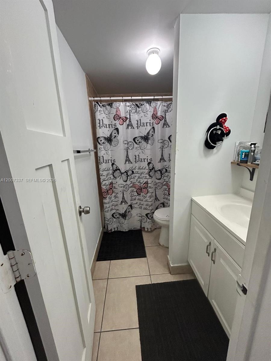 A small bathroom features a white vanity, a Paris-themed shower curtain, and beige floor tiles — 1100 NE 1st Ct # 104, Hallandale Beach FL 33009, HALLANDALE BEACH, FL