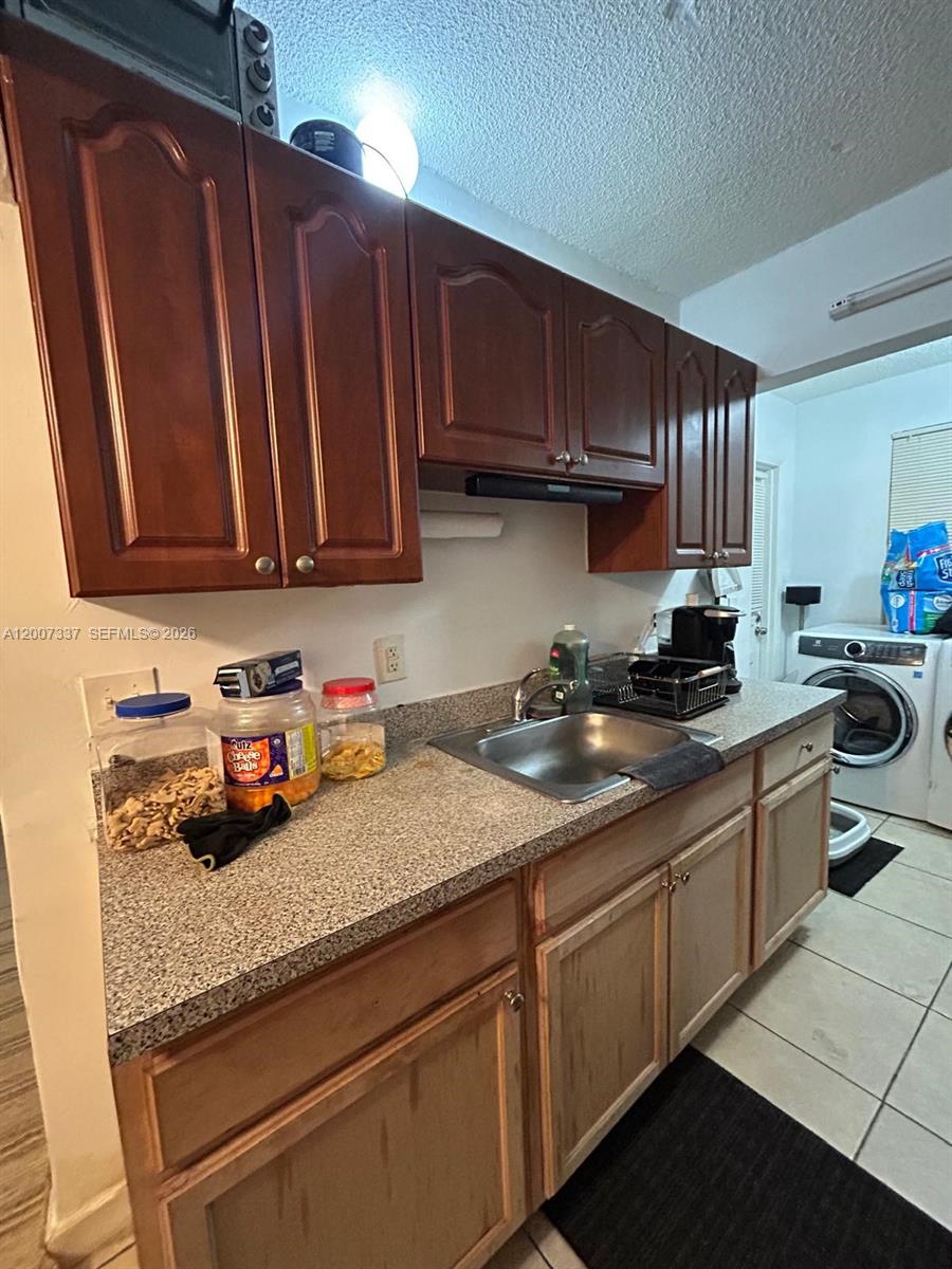 A kitchen features wood cabinets, a stainless steel sink, and a front-loading washing machine — 1100 NE 1st Ct # 104, Hallandale Beach FL 33009, HALLANDALE BEACH, FL