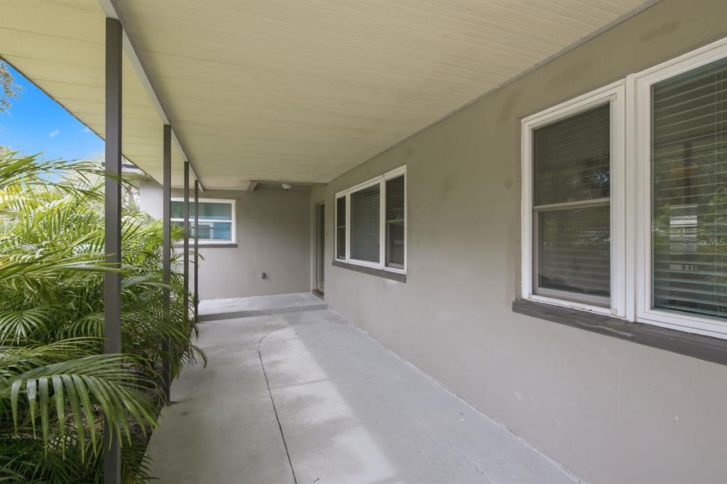 A covered concrete patio runs along the side of a house with gray walls — 1626 S BETTY LANE, CLEARWATER, FL