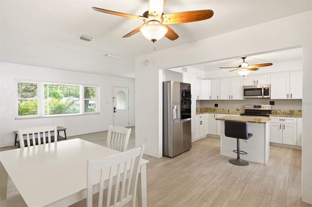 An open-concept kitchen and dining area features white cabinetry, stainless steel appliances, and wood-look flooring — 1626 S BETTY LANE, CLEARWATER, FL