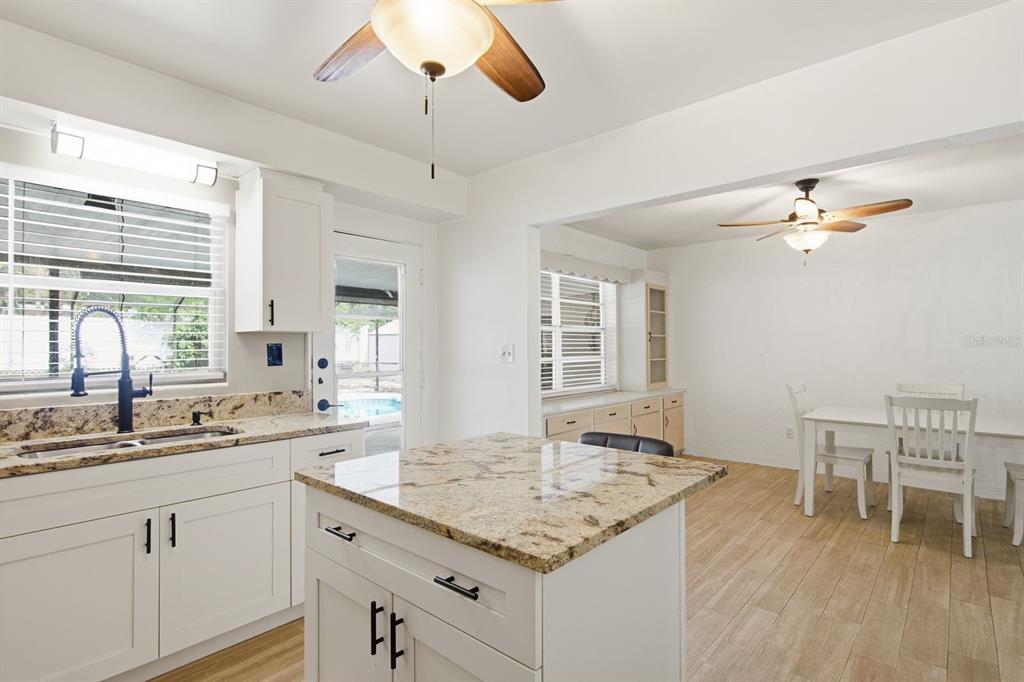 A kitchen with white cabinets, granite countertops, and an island opens into a dining area — 1626 S BETTY LANE, CLEARWATER, FL