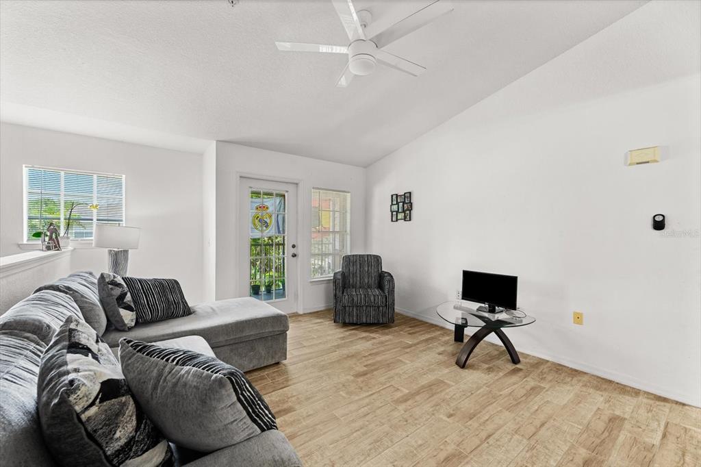 A living room features a grey sectional sofa, a glass coffee table, and wood-look flooring — 8933 MANOR LOOP UNIT 204, LAKEWOOD RANCH, FL
