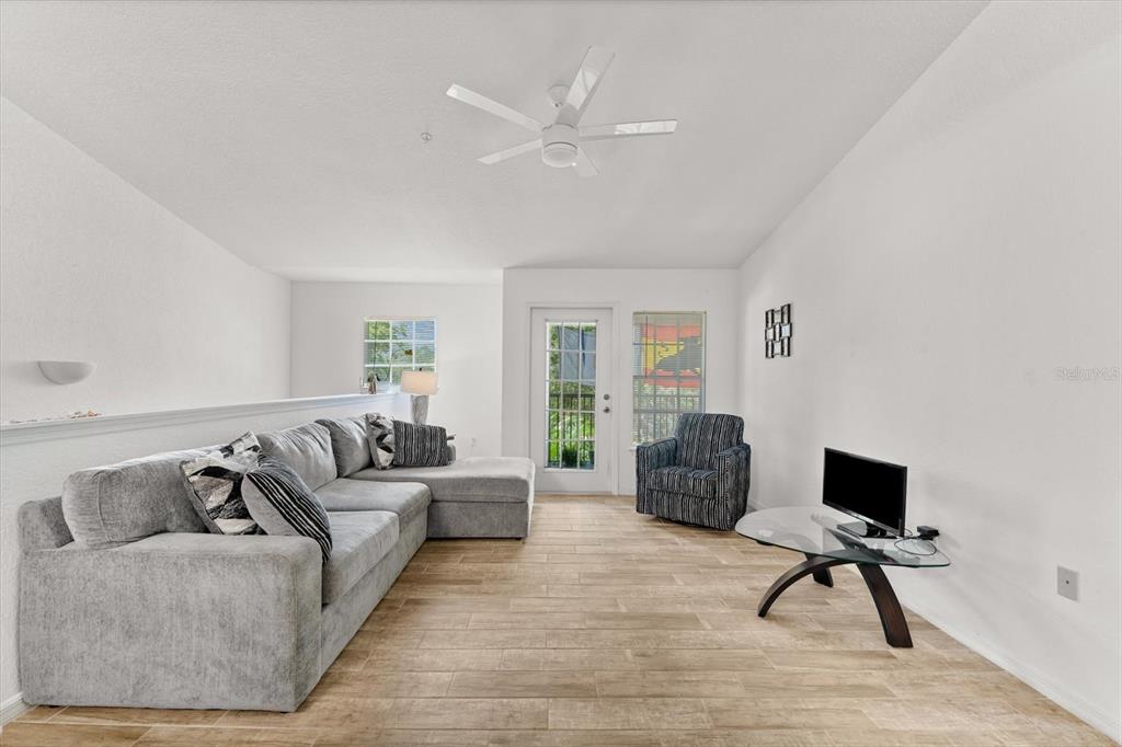 A living room features a grey sectional sofa, a glass coffee table, and tile flooring — 8933 MANOR LOOP UNIT 204, LAKEWOOD RANCH, FL