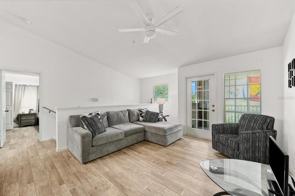 A living room features a gray sectional sofa, a striped armchair, and light wood flooring — 8933 MANOR LOOP UNIT 204, LAKEWOOD RANCH, FL