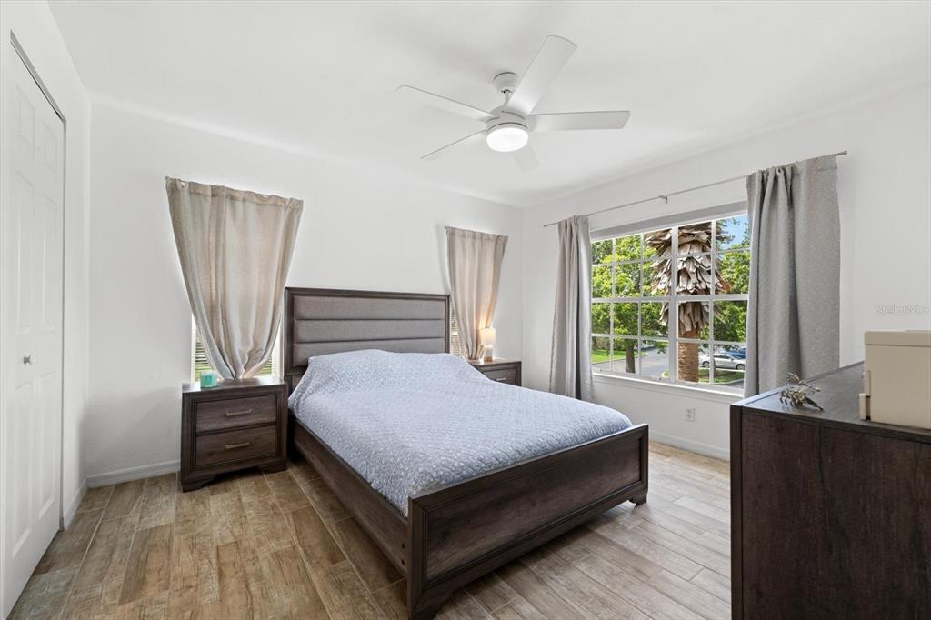 A bedroom features a bed with a gray headboard, wood-look tile flooring, and two windows — 8933 MANOR LOOP UNIT 204, LAKEWOOD RANCH, FL