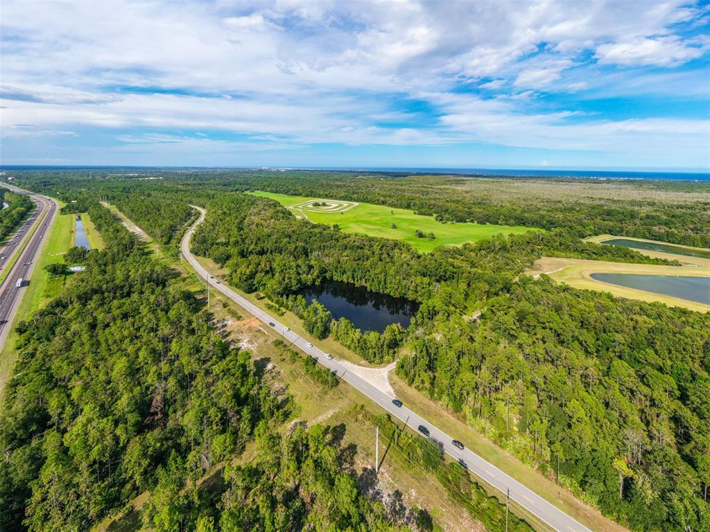 An aerial view shows a road running through a wooded area with a small pond — xx OLD KINGS ROAD, PALM COAST, FL