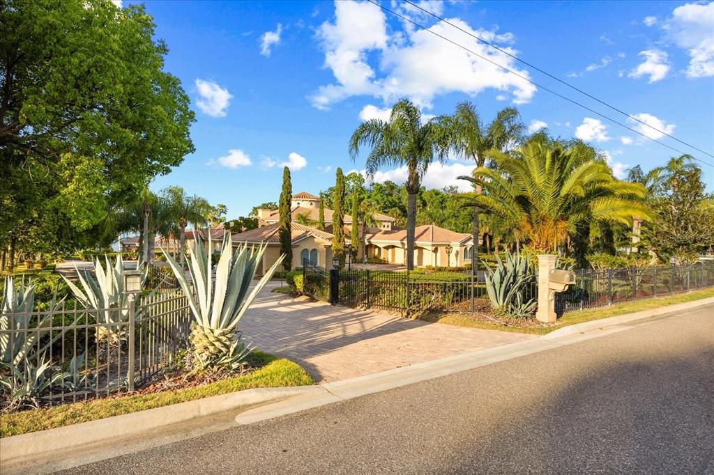 A gated driveway leads to a Mediterranean-style house surrounded by palm trees and agave plants — 1112 ORANGE AVENUE, WINTER SPRINGS, FL