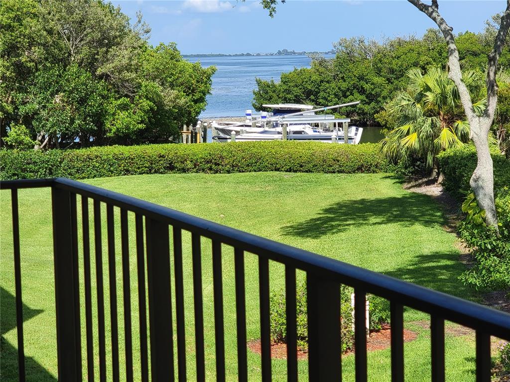 A view from a balcony overlooking a grassy lawn, trees, and a boat in the water — 1515 PINELLAS BAYWAY S UNIT 38, TIERRA VERDE, FL