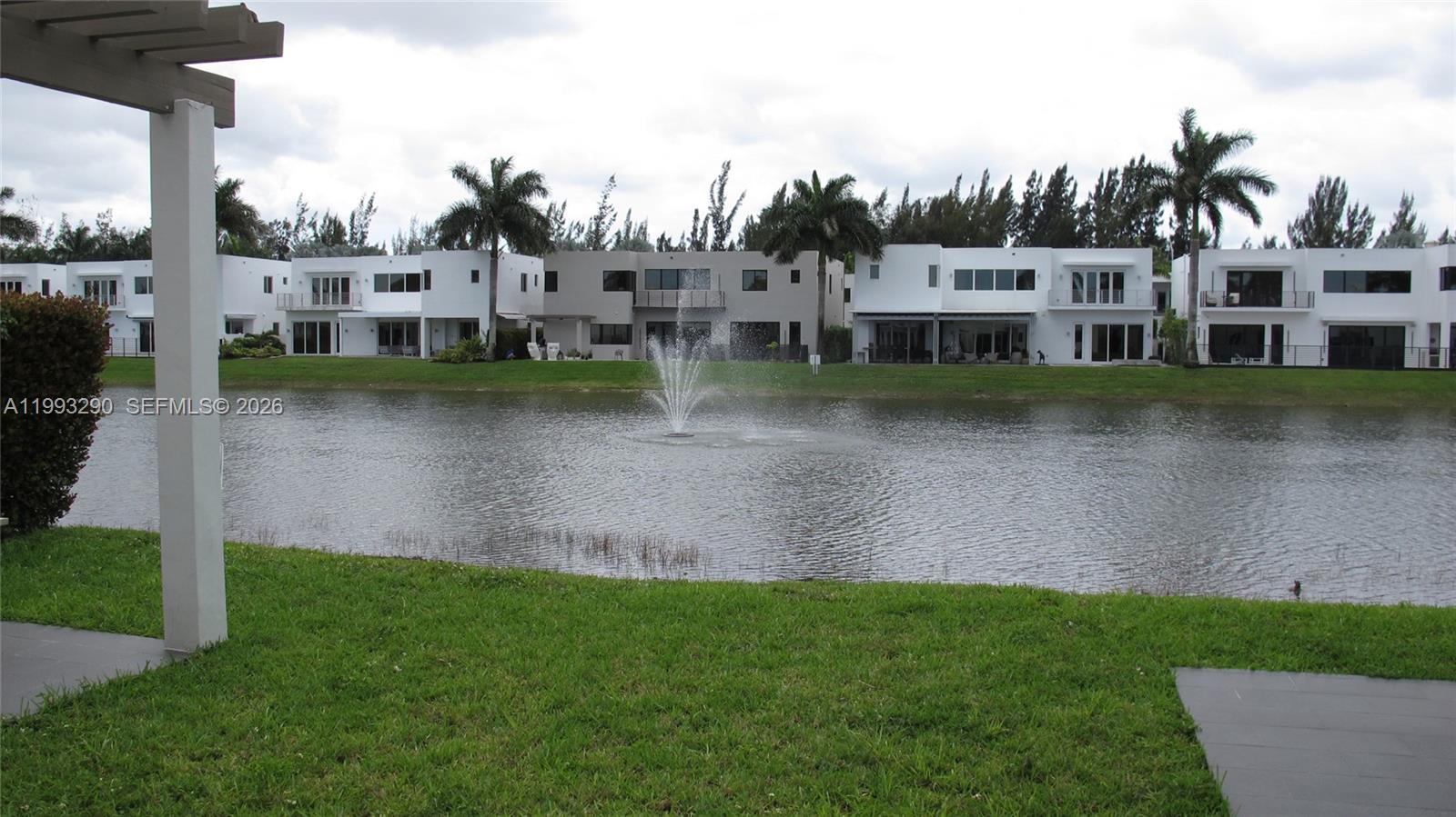 A pond with a fountain sits in front of several modern white houses — 10272 NW 75th Ter, Doral FL 33178, DORAL, FL