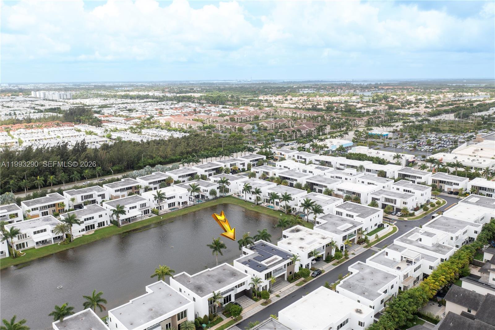 An aerial view shows a modern residential complex with white townhomes surrounding a central lake — 10272 NW 75th Ter, Doral FL 33178, DORAL, FL