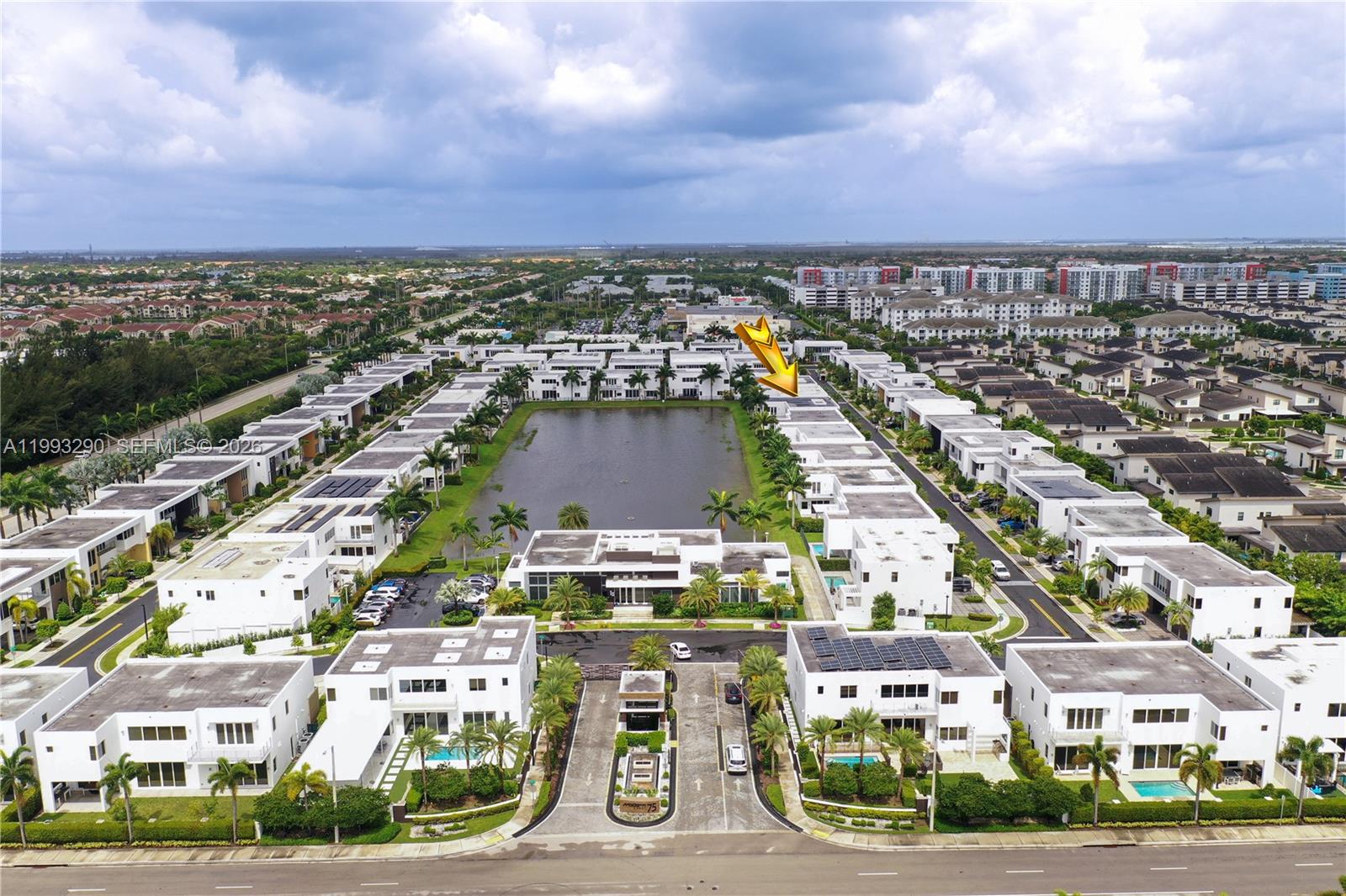 An aerial view shows a gated residential community with white townhouses surrounding a central pond — 10272 NW 75th Ter, Doral FL 33178, DORAL, FL