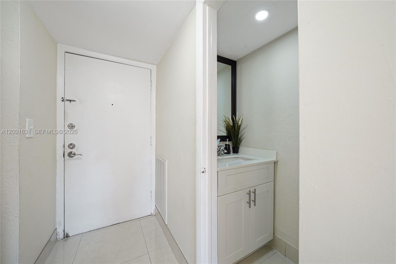 A white front door stands next to a small bathroom with a vanity and mirror — 1305 W 53rd St # 429, Hialeah FL 33012, HIALEAH, FL